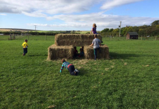 Niños juegan en pacas de heno al aire libre bajo el cielo azul en Feather Down Warren Farm, Suroeste de Inglaterra.