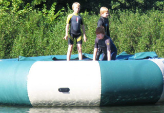 Drie kinderen spelen op een groot opblaasbaar waterplatform bij Upper Shadymoor Farm in Wales, VK.