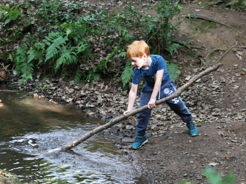 Jongen speelt met een lange stok bij een beekje bij Feather Down Upper Shadymoor Farm in Wales, Verenigd Koninkrijk.