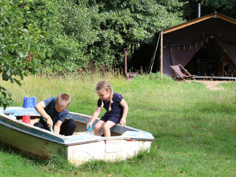 Dos niños juegan en un bote lleno de arena junto a una tienda en Feather Down Upper Shadymoor Farm, Gales.