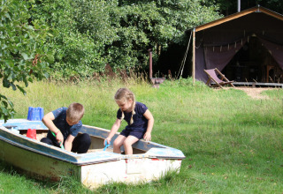 Zwei Kinder spielen in einem Sandkastenboot auf einer Wiese, im Hintergrund ein Zelt auf Upper Shadymoor Farm.
