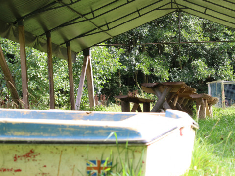 Covered area at Feather Down Upper Shadymoor Farm, Wales with rustic benches, table, and boat in grass.