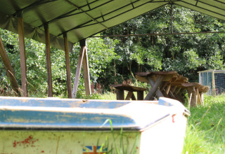 Überdachter Bereich auf Feather Down Upper Shadymoor Farm in Wales mit Tisch, Bänken und Boot im Gras.