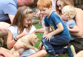 Kinderen en volwassenen spelen met een puppy op Feather Down Upper Shadymoor Farm, een vakantiepark in Wales.