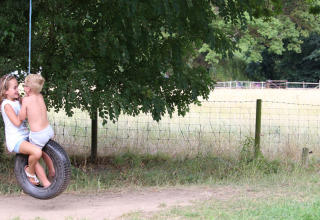 Two children playing on a tire swing under a tree at Feather Down Upper Shadymoor Farm in Wales, United Kingdom.