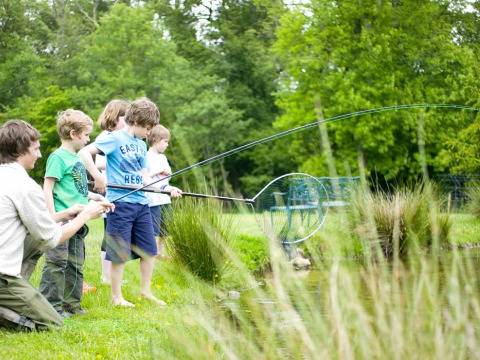 Kinderen en volwassene vissen aan het water op Feather Down Upper Shadymoor Farm in Wales, Verenigd Koninkrijk.