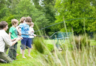 Children and an adult fishing by a pond surrounded by greenery at Feather Down Upper Shadymoor Farm in Wales.
