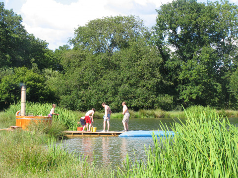 Children playing on a wooden raft in a scenic lake setting at Feather Down Upper Shadymoor Farm, Wales, UK.