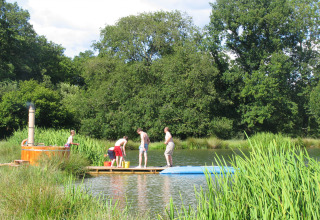 Children playing on a wooden raft in a scenic lake setting at Feather Down Upper Shadymoor Farm, Wales, UK.
