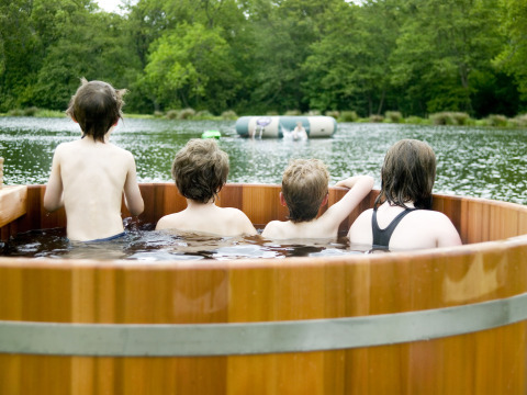 Vier kinderen genieten samen in een houten hottub met zicht op het meer in een vakantiepark in Wales, VK.