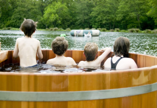 Vier kinderen genieten samen in een houten hottub met zicht op het meer in een vakantiepark in Wales, VK.