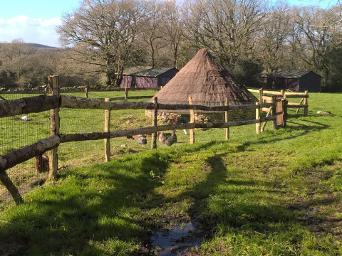 Casa tradicional circular con techo de paja y cercado en un campo verde en Feather Down La Ferme de Penquelen Huella.