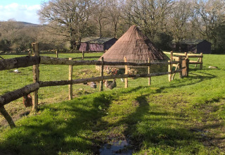 Billede af et traditionelt stråtagshus, indhegnet på en grøn mark ved Feather Down La Ferme de Penquelen Huella.