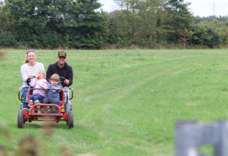 En familie cykler på en firehjulet cykel gennem en grøn mark ved Feather Down New Barn Farm i England.