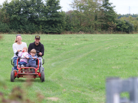 Familie fährt auf einem Vier-Personen-Fahrrad über eine grüne Wiese bei Feather Down New Barn Farm, England.