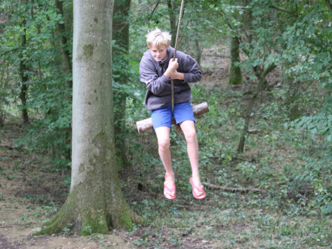 Child swinging on a rope swing in a woodland at Feather Down New Barn Farm holiday park, East of England, UK.