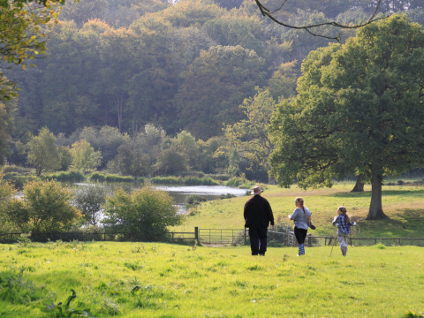 Una famiglia cammina su un prato verde a Feather Down Manor Farm, con alberi e un lago nel sud-est dell'Inghilterra.