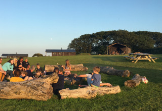 Famiglie e bambini seduti su tronchi a Feather Down Treganhoe Farm, un parco vacanze nel sud-ovest dell'Inghilterra.