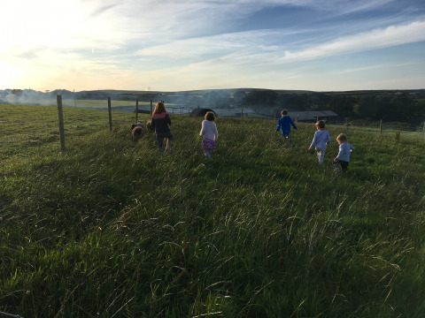 Kinderen rennen door hoog gras bij zonsondergang op Feather Down Treganhoe Farm in Zuidwest-Engeland.