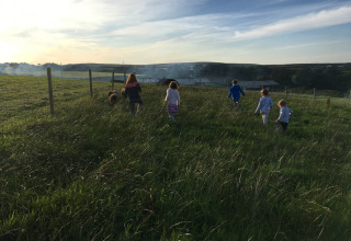 Kinderen rennen door hoog gras bij zonsondergang op Feather Down Treganhoe Farm in Zuidwest-Engeland.