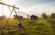 Kinderen spelen op een schommel en trampoline bij huisjes op Feather Down Hoeve den Overdraght in West-Vlaanderen.