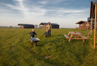 En familie på glamping med børn, der leger med en trillebør på grønne marker ved feriehytter i Belgien.