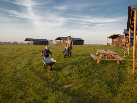 Des enfants jouent avec une brouette sur une prairie devant des cabanes au parc de vacances en Belgique.