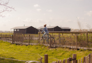 Kvinde cykler langs et hegn i Feather Down Hoeve den Overdraght feriepark i Vestflandern, Belgien.