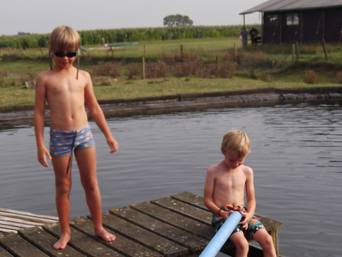 Dos niños juegan en un muelle de madera junto al agua en Feather Down Hoeve den Overdraght, West Flandes, Bélgica.