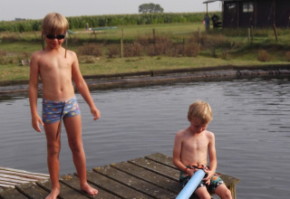 Twee kinderen spelen op een houten steiger aan het water bij Feather Down Hoeve den Overdraght in West-Vlaanderen.