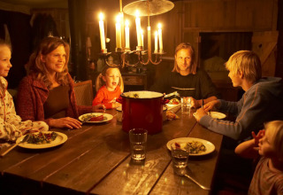En familie sidder sammen ved et træbord og nyder et aftenmåltid under stearinlys i et hyggeligt rum.
