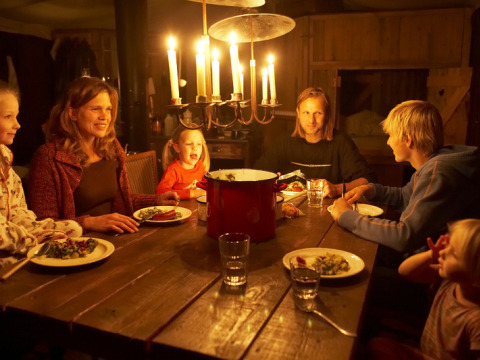 A family gathers around a rustic wooden table for a candlelit dinner in a cozy room at holiday park.