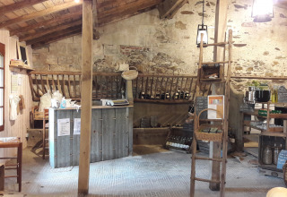 Interieurfoto van een rustieke winkel met houten meubels, stenen muren, schappen en warme verlichting.