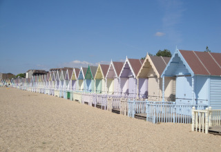 Casette da spiaggia colorate sulla sabbia sotto il cielo blu a Feather Down Layer Marney Tower, Inghilterra orientale.