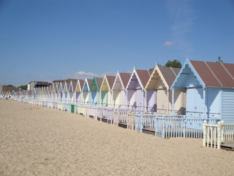 Colorful beach huts lined up on sandy beach under blue sky at Feather Down Layer Marney Tower, East England.