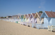 Bunte Strandhütten an einem Sandstrand unter blauem Himmel in Feather Down Layer Marney Tower, Ostengland.