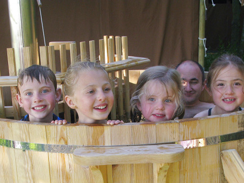 Kinderen en een volwassene genieten van een houten buitenspa bij Feather Down Layer Marney Tower in Engeland.