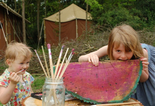 Due bambini giocano con pennelli e un tronco dipinto all’aperto a Feather Down Layer Marney Tower.