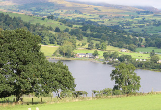 Udsigt over grønne bakker, sø og gårdhuse ved Feather Down Pant y March Farm feriepark i Wales, Storbritannien.
