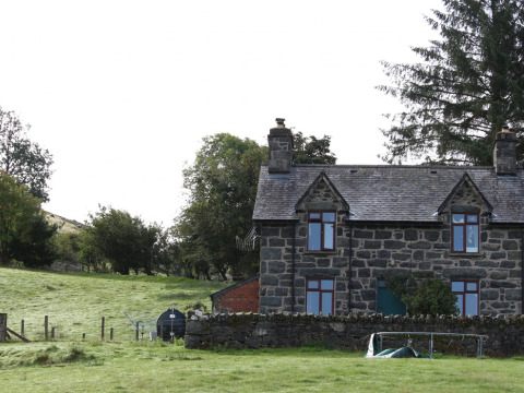 Casa de piedra en Feather Down Pant y March Farm, rodeada de prados verdes y árboles en Gales, Reino Unido.