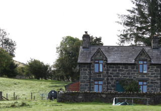 Stenhus ved Feather Down Pant y March Farm feriepark omgivet af grønne marker og træer i Wales, Storbritannien.