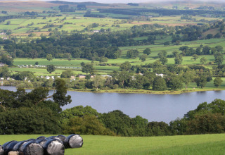 Scenic view of Welsh countryside at Feather Down Pant y March Farm, showing fields, trees, and a tranquil lake.