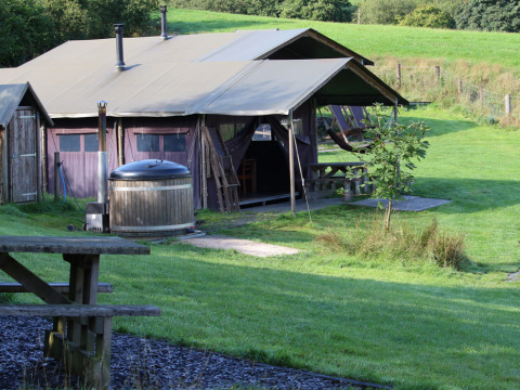 Glamping-Zelt mit Terrasse, Whirlpool und Sitzbereich auf Feather Down Pant y March Farm in Wales, Großbritannien.