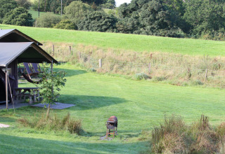 Panorama af Feather Down Pant y March Farm i Wales med grønne marker, teltlejr og grill under åben himmel.