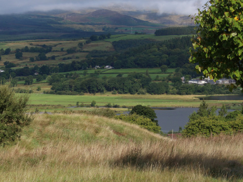 Vista del campo galés desde Feather Down Pant y March Farm, con colinas verdes y un lago cercano.