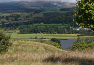 Landschap aan Feather Down Pant y March Farm in Wales met groene weiden, heuvels en een meer.