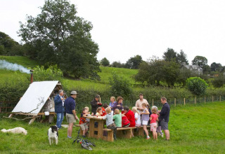 Families en vrienden aan tafel genieten buiten op Feather Down Pant y March Farm, Wales, omgeven door natuur.