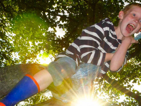 Jongen in gestreept shirt en blauwe laarzen buitenspelend op Feather Down Pant y March Farm, Wales, met zonlicht.