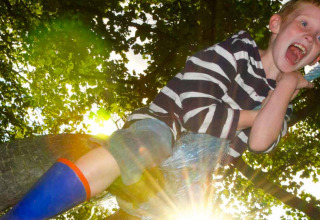 Ragazzo con maglia a righe e stivali blu gioca all’aperto a Feather Down Pant y March Farm, Galles, sotto il sole.