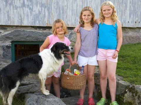 Tres niñas y un perro con una cesta frente a un granero en Feather Down Pant y March Farm en Gales, Reino Unido.